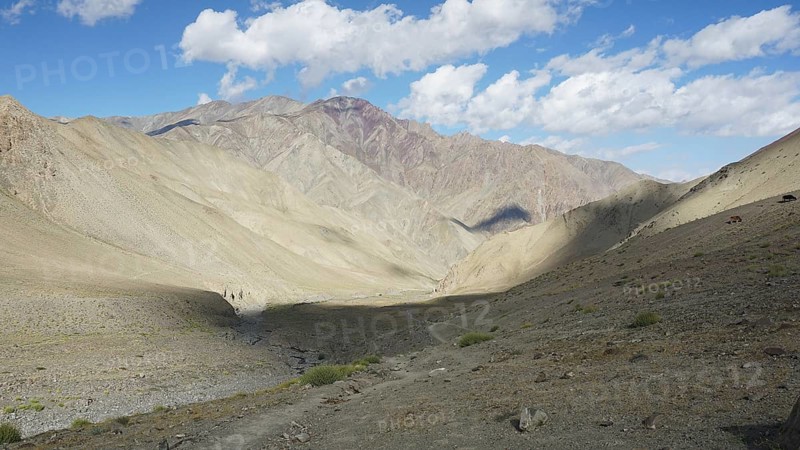 Wide mountain valley under a partly cloudy sky with a small path, trekking in Ladakh, Stok la, Himalayas, India