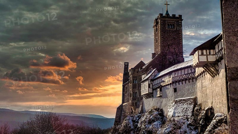 Snowy Wartburg in Eisenach in front of a picturesque and dramatic sky in romantic colors, at dusk, sunset, hiking on the Rennsteig, Thuringian Forest nature park Park