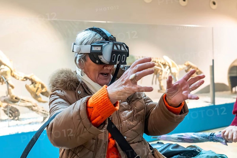 Senior woman wearing a vr headset reaching out with her hands, interacting with a virtual environment in a modern museum, engaging with new technology
