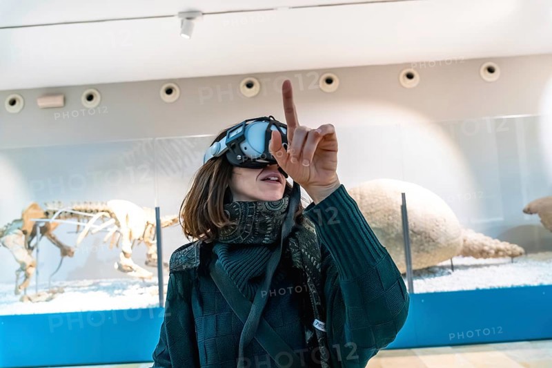 Woman wearing a vr headset interacting with virtual elements and exploring an augmented reality exhibition, enhancing her learning experience around dinosaur skeletons and ancient fossils