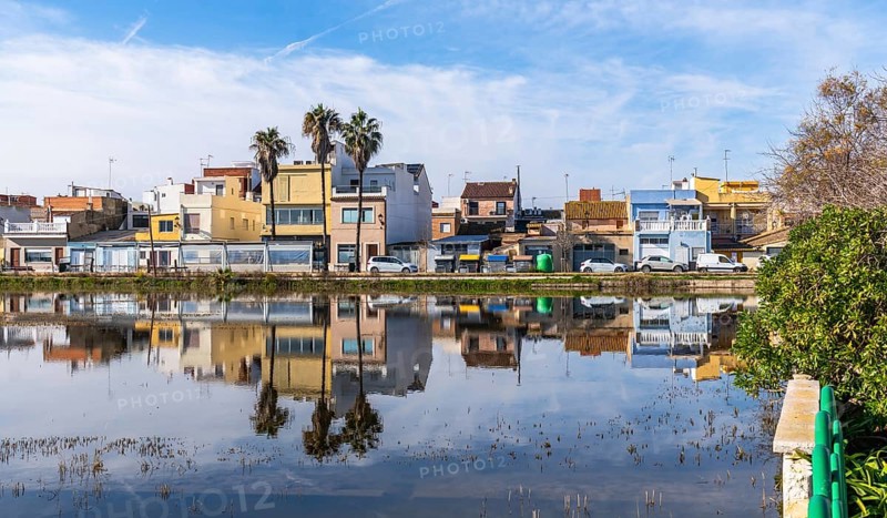 El palmar fishing village houses and palm trees mirrored in the calm albufera lake under a vivid blue sky, traditional waterfront architecture in valencia, spain