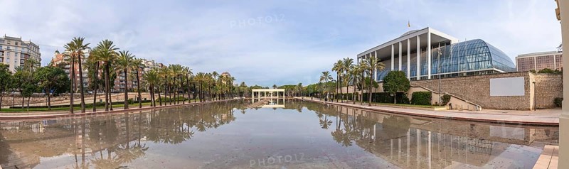 Palau de la musica, a modern architectural landmark, reflecting in the tranquil waters of the turia gardens park, with palm trees lining the long promenade in valencia, spain