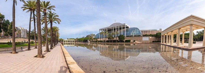 Palau de la musica concert hall architecture reflecting in a calm water pond, surrounded by palm trees and landscaped gardens on a sunny day in valencia, spain