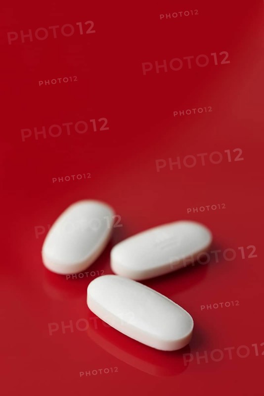 A minimalist image featuring three oblong white tablets, subtly embossed, isolated against a deep red background with a soft focus setting