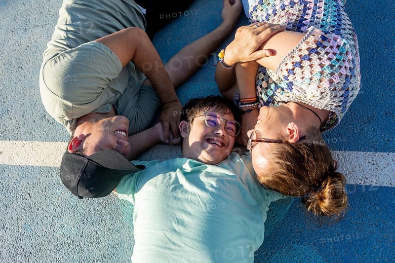 A teenager with Down Syndrome lying outdoors with family, enjoying a loving and joyful moment together Their smiles and relaxed demeanor showcase a strong family bond