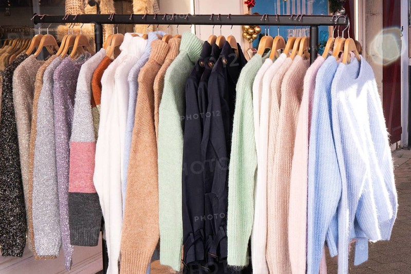 A collection of cozy wool and knit sweaters in various colors and textures hangs neatly on wooden hangers in a clothing store, showcasing stylish winter fashion trends