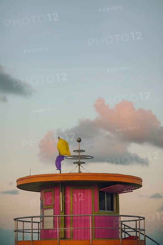 A picturesque view of a vibrant, colorful lifeguard tower on Miami Beach, captured under a softly lit sky at sunset. This image features pastel colors and a serene background