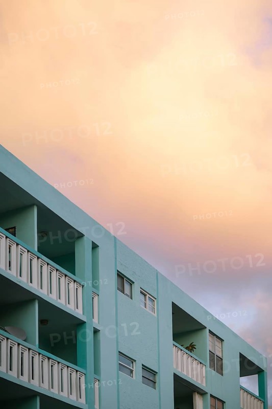 Soft sunset colors bathe a Miami Beach building, rendering the sky in warm peach tones above the cool mint green structure