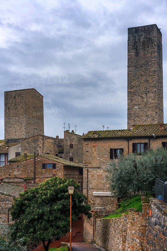 A panoramic view of San Gimignano, highlighting its famous medieval towers and traditional stone buildings. The lush greenery and cloudy sky add to the timeless beauty of Tuscany