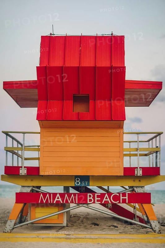 Vibrant red and orange lifeguard stand prominently positioned on Miami Beach, captured during a cloudy day, showcasing the unique architecture and eye-catching colors against a serene beach background