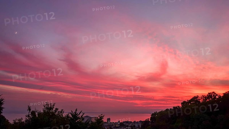 Captivating view of a vivid sunset painting the skies in shades of pink and red, over Lausanne and Lake Leman, highlighting the serene landscape and tranquil waters