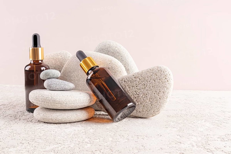 Two amber glass serum bottles with golden caps are artfully displayed among smooth gray stones, evoking a serene and spa-like ambiance for relaxation and skincare