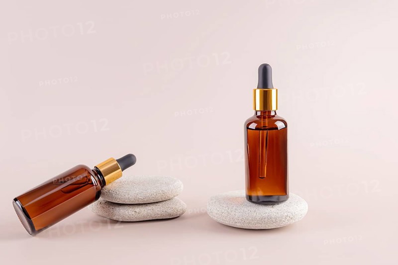 Two amber glass dropper bottles on smooth stones, featuring a minimalist aesthetic Ideal for showcasing oils or skincare products on a neutral background