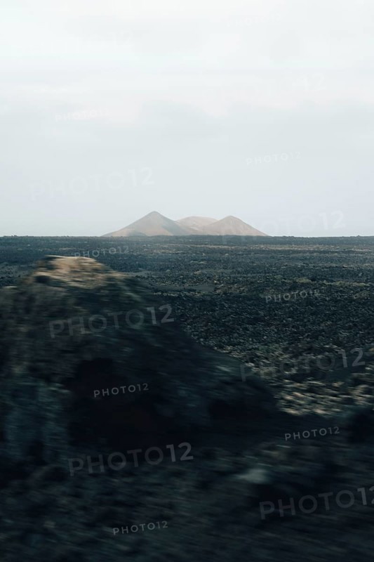 Serene Lanzarote landscape featuring vast volcanic plains and distant, hazy mountains under a muted sky, capturing the barren beauty and mystique of the island
