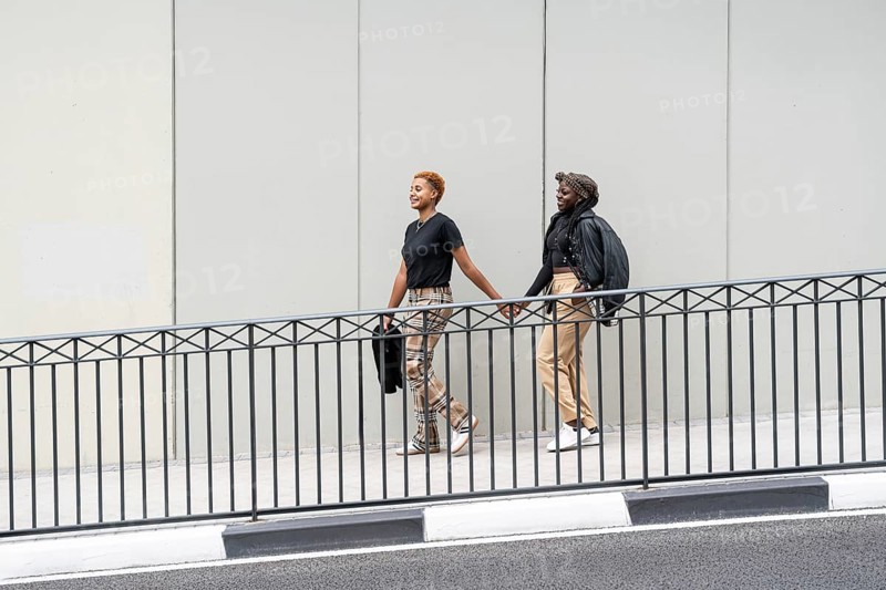Two people walk hand in hand, smiling outdoors, expressing love and unity as a multiethnic couple. Casual attire, urban setting, showcasing an uplifting scene of connection
