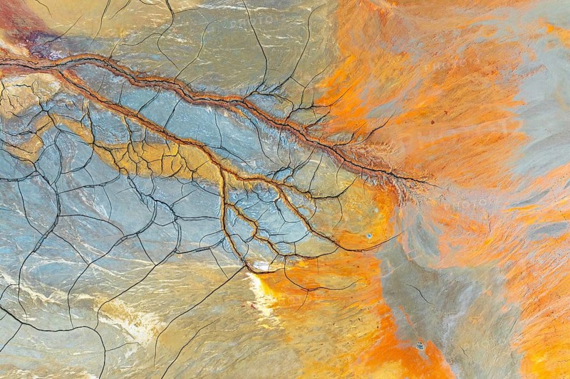 Aerial perspective of vibrant multicolor mud patterns and textures The image showcases natural, flowing designs in earthy tones of orange, blue, and brown, intersected by fine lines