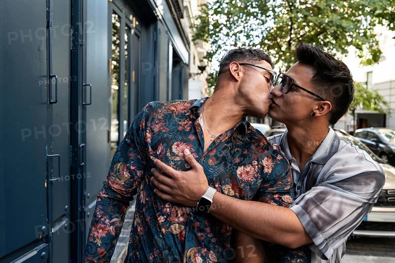 A latin gay couple shares a tender kiss on a lively street in Madrid, capturing a moment of love and connection in an urban setting with vivid colors and natural light