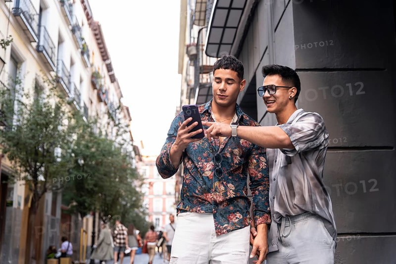 A joyful latin gay couple using a smartphone while strolling through a vibrant street in Madrid, Spain. They share a moment of connection and exploration in the bustling city