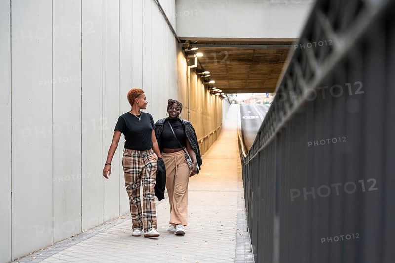 A joyful LGBT multiethnic couple walks side by side through a well-lit urban underpass, sharing a moment of happiness and connection in a modern cityscape