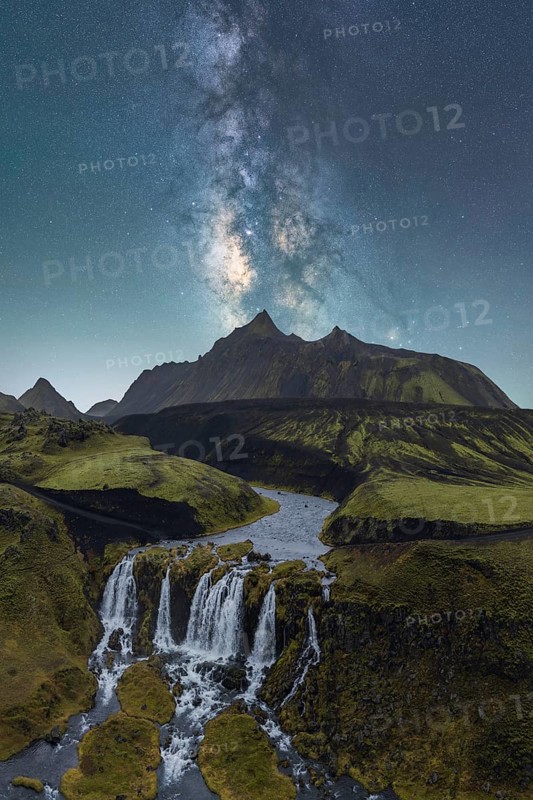 A breathtaking view of the Milky Way illuminating the night sky over a lush Icelandic landscape, featuring a cascading waterfall and rugged mountains under the starry expanse