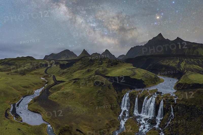 Captivating Icelandic scene with a lush green landscape, a winding river, and a cascading waterfall, set beneath a mesmerizing star-filled night sky