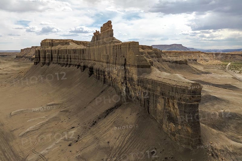 A dramatic aerial view of Caineville Mesa, Utah, showcasing towering rock formations and expansive desert landscape under a partly cloudy sky A testament to nature's grandeur