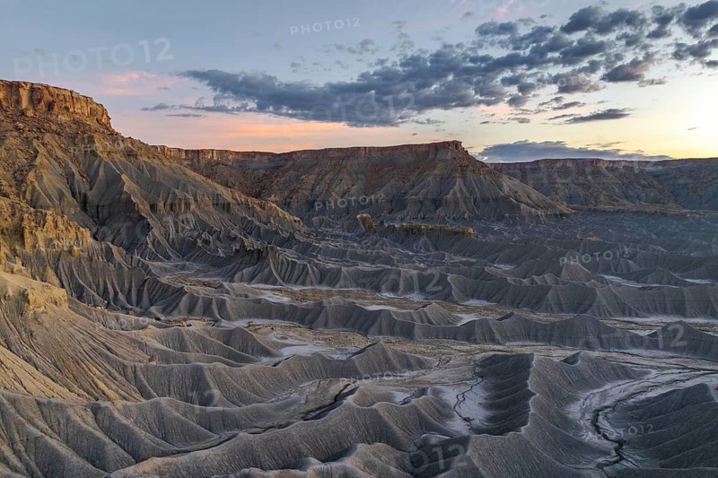 A stunning view of Caineville Mesa, Utah, showcasing dramatic geological formations under a vibrant sunset sky The scene captures the rugged beauty of this iconic landscape