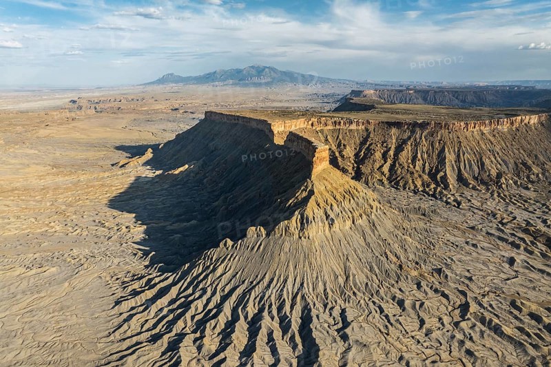 Dramatic aerial view of Caineville Mesa in Utah, USA, showcasing rugged terrain, layered rock formations, and expansive desert vistas under a vast sky