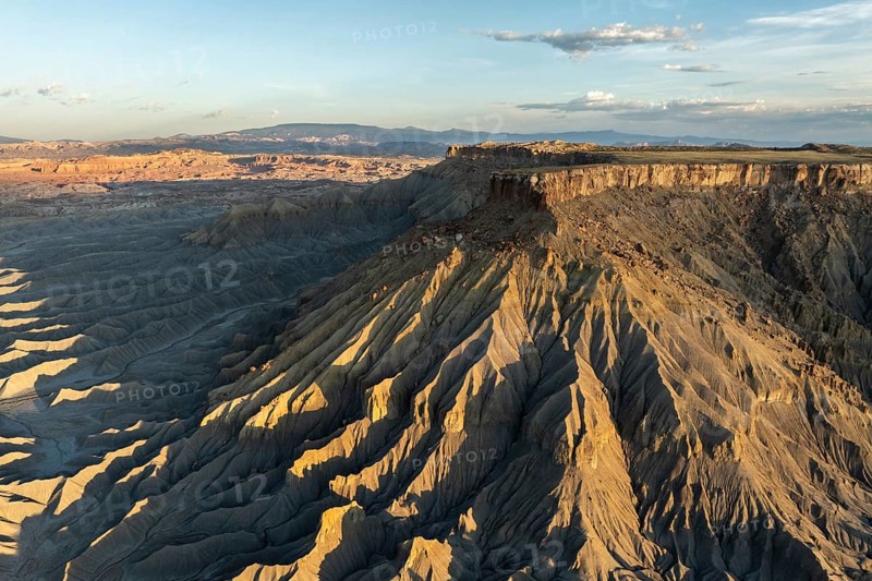 Aerial view of Caineville Mesa, Utah, showcasing dramatic ridges and rocky terrain under a clear sky The golden light accentuates the unique formations of this desert region