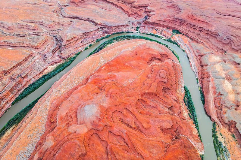 Stunning aerial shot capturing the sinuous Rio San Juan winding through the dramatic red rock formations in Utah, USA. The vibrant orange and red hues contrast vividly with the lush green riverbanks