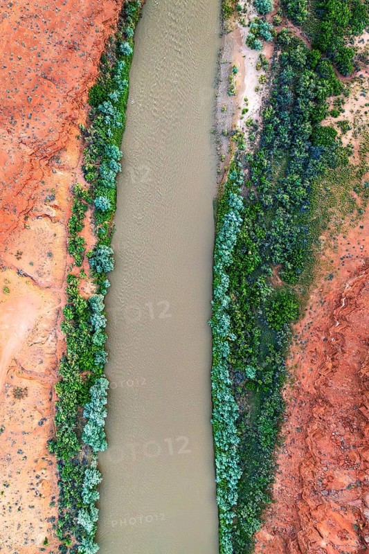 A striking aerial shot of the Rio San Juan winding through vibrant red rock landscapes, contrasted by lush greenery on its banks in Utah, USA