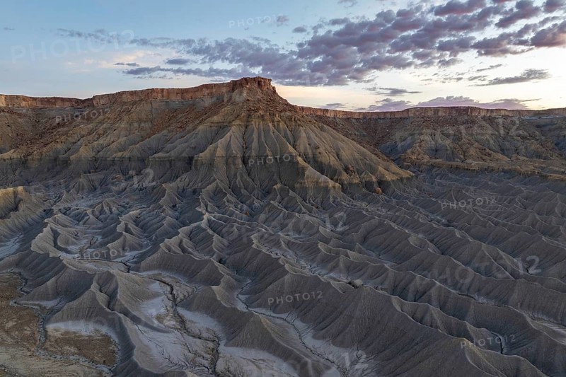 Captivating vista of Caineville Mesa in Utah, USA, showcasing dramatic rugged terrain and striking geological formations under a colorful sunset sky, ideal for nature enthusiasts