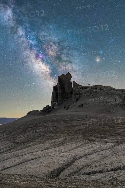 Unrecognizable person silhouette stands on a rugged Utah desert terrain under a vivid Milky Way. The celestial scene captures glowing stars against a stark landscape, highlighting nature's beauty