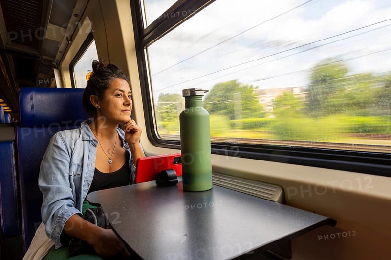 A thoughtful passenger gazes out a train window, absorbing the scenic landscape Sunlight filters through, creating a tranquil atmosphere perfect for travel reflection and relaxation