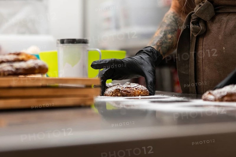 A skilled baker with tattooed arms wearing gloves arranges freshly baked pastries on a counter The warm and inviting ambiance reflects an authentic Italian bakery scene