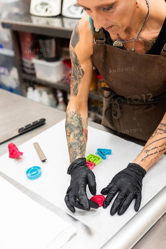 A skilled artisan in an Italian bakery decorates fondant Wearing gloves and an apron, they craft colorful shapes, embodying creativity and precision in a bustling kitchen