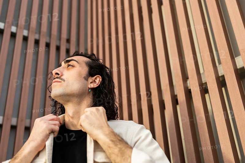 A man gazes upward with confidence, adjusting his collar against a modern architectural backdrop The image reflects a contemporary lifestyle and urban fashion sense