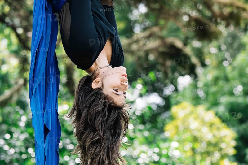 Aerial acrobat performs elegant moves on blue fabric amidst lush greenery in a Bogota park The dynamic pose and vibrant colors highlight the harmony of nature and art