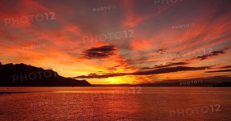 A breathtaking sunset over Lake Geneva, illuminated with vibrant shades of orange and red, with the silhouette of the Swiss Alps in the background