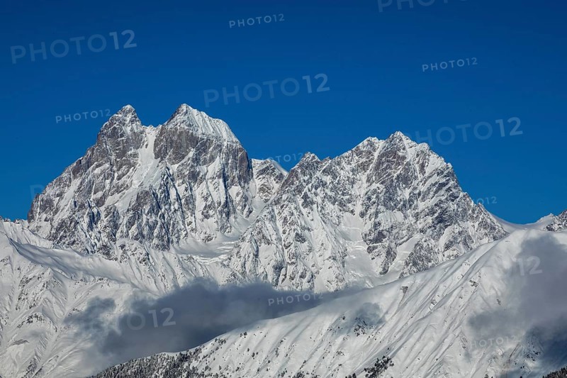 Majestic snow-covered mountain peaks tower under a clear blue sky, creating a breathtaking natural scene in Georgia Shadows and clouds add contrast to the pristine white snow
