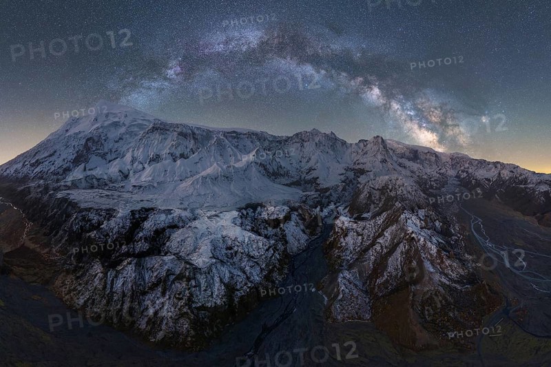 Stunning view of Icelandic mountains blanketed in snow, illuminated by a dazzling starry night sky The Milky Way arches above, showcasing nature's serene beauty