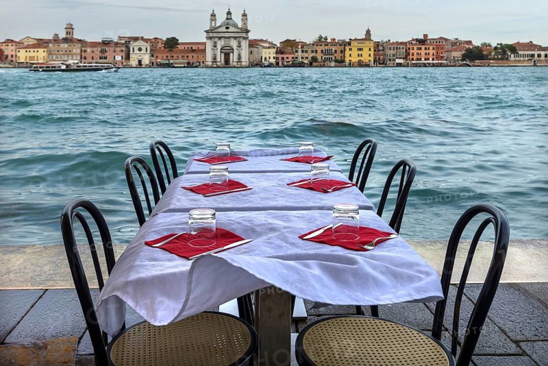 Restaurant tables on the shore in windy weather, on the island of Giudecca, Venice behind, Veneto, Italy