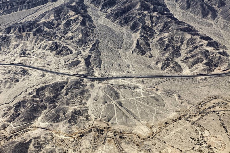 Dry, rocky desert landscape with lines and a highway, the geoglyphs and images in the desert near Nasca and Palpa in Peru