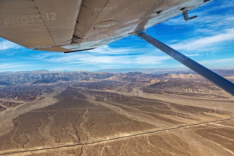 View from an airplane over desert and mountains under a blue sky, the desert landscape near Nasca in Peru