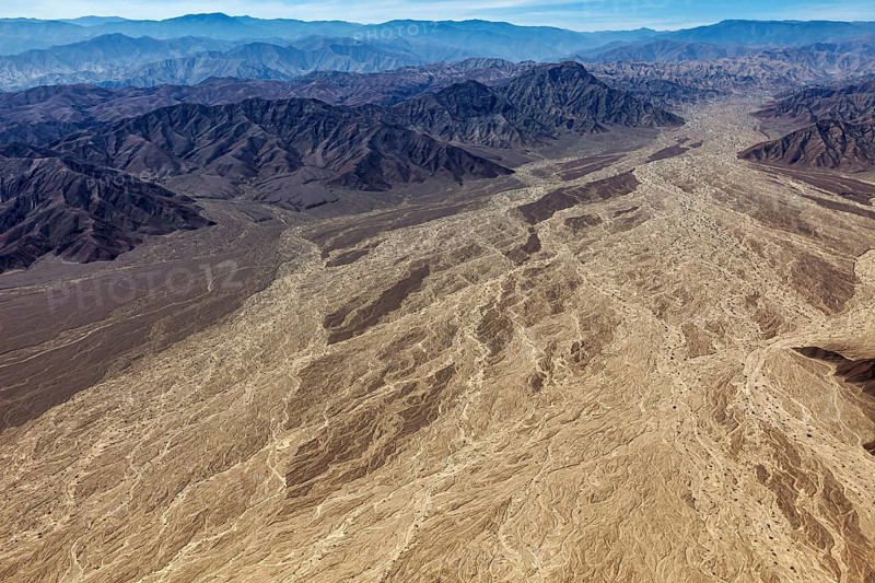 Large-scale desert landscape with a complex pattern of dry river beds surrounded by a mountain range under clear skies, The desert landscape near Nasca in Peru