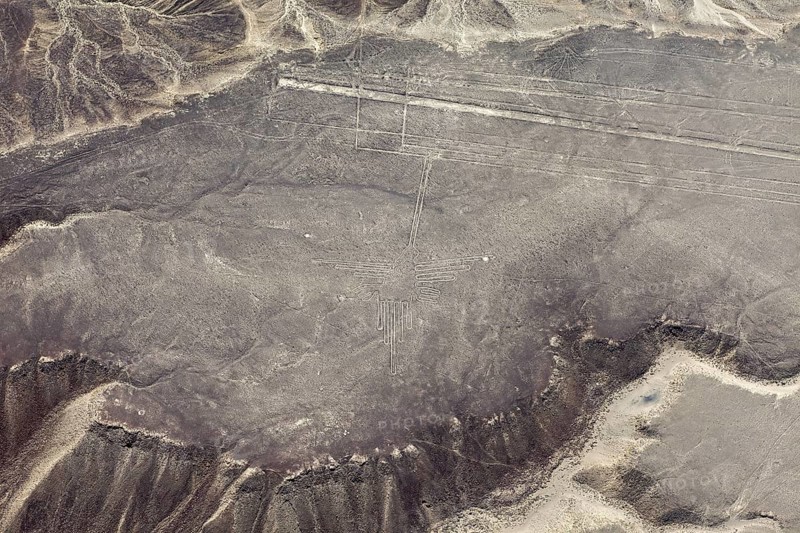 A pictogram surrounded by geoglyph lines in a sandy desert area, viewed from the air with surrounding mountains, the geoglyphs and images in the desert near Nasca and Palpa in Peru