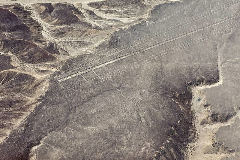 Geoglyph lines in an extensive, sand-colored desert landscape with nearby mountains, the geoglyphs and images in the desert near Nasca and Palpa in Peru