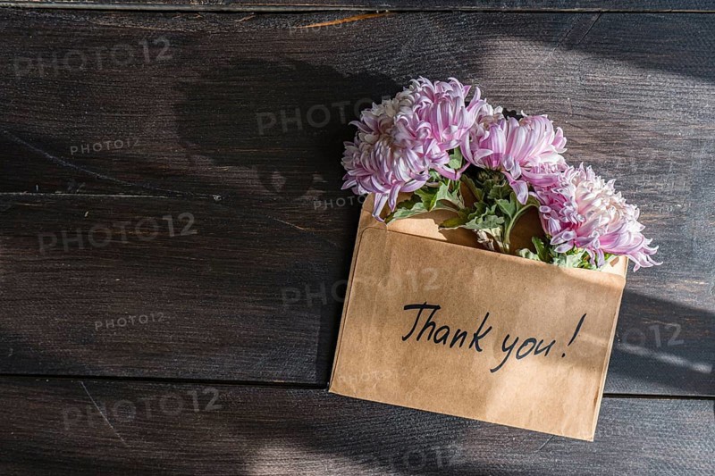 A brown envelope with Thank you written on it holds pink chrysanthemums The flowers rest gracefully on a dark wooden surface, complimenting the fall aesthetic