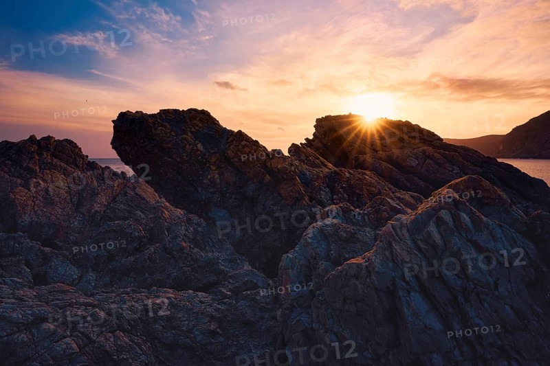 At Cala del Lastre, Portman in Murcia, Spain, a breathtaking sunset casts warm hues over rugged rocks, creating a stunning coastal view that embraces nature's beauty