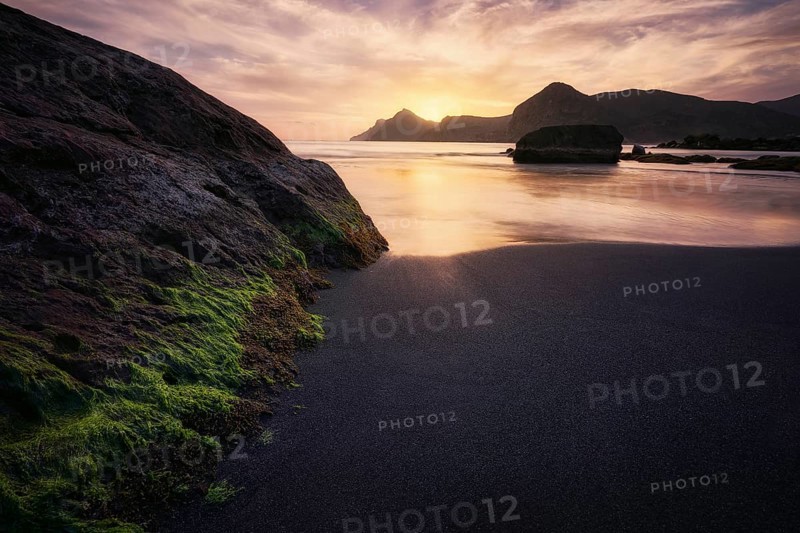 The tranquil sunset casts a golden hue over the rugged rocks and calm waters of Cala del Lastre in Murcia, Spain, creating a peaceful and scenic coastal view